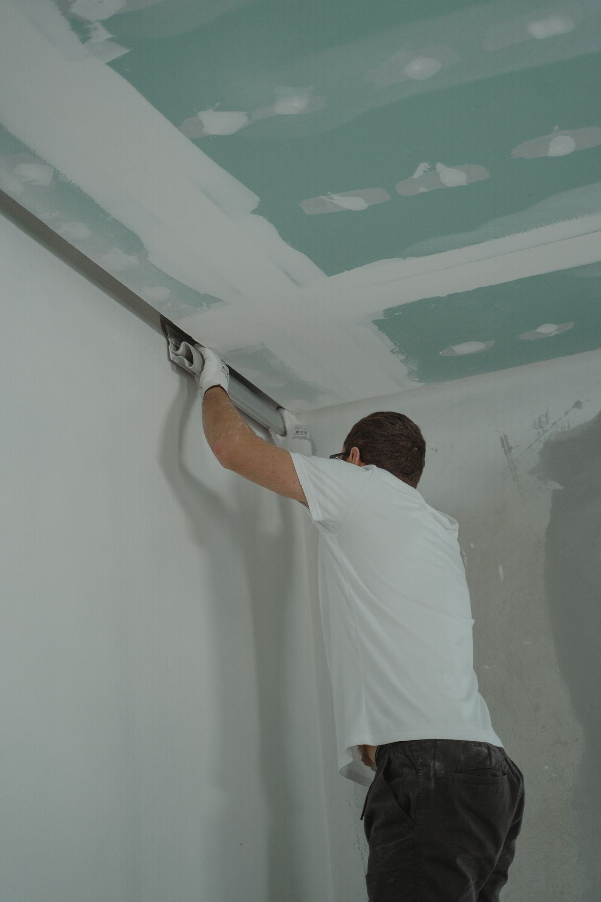Contractor smoothing joint compound along the edge where a drywall ceiling meets the wall