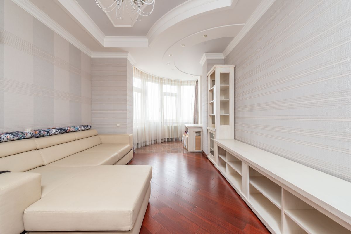 Long living room with a smooth white ceiling, cove lighting details, and wood flooring